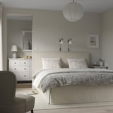 Modern bedroom with gray TÄRNKULLEN bed, floral patterns, and armchair. Serene, cozy ambiance.