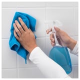 A person holds a blue TISKEN towel rack with a blue cloth, attaching it to white tiled wall using suction cups.