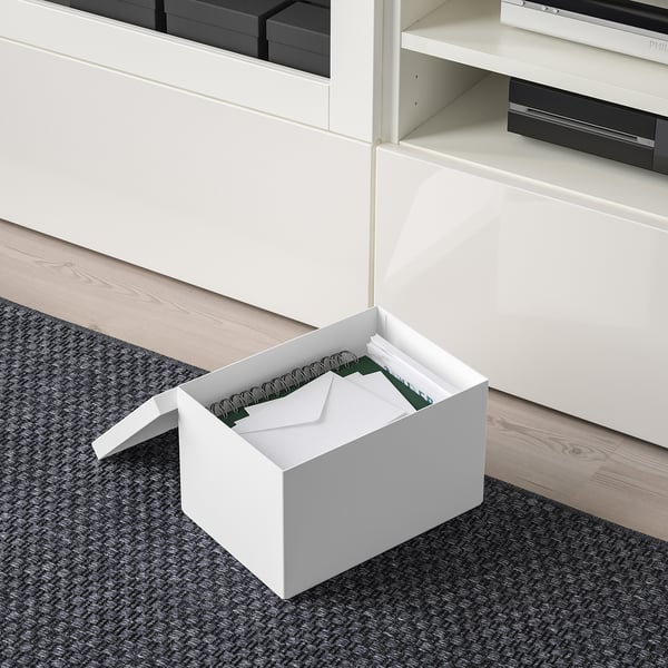 White TJENA box, open with papers, under white shelves. Neat storage solution.