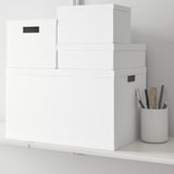 Stacked white storage boxes on desk, ideal for organizing small items. Boxes are from TJENA series by ikea, suitable for workspaces.