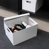 Open white TJENA storage box with headphones and gadgets, ideal for organizing desk accessories.