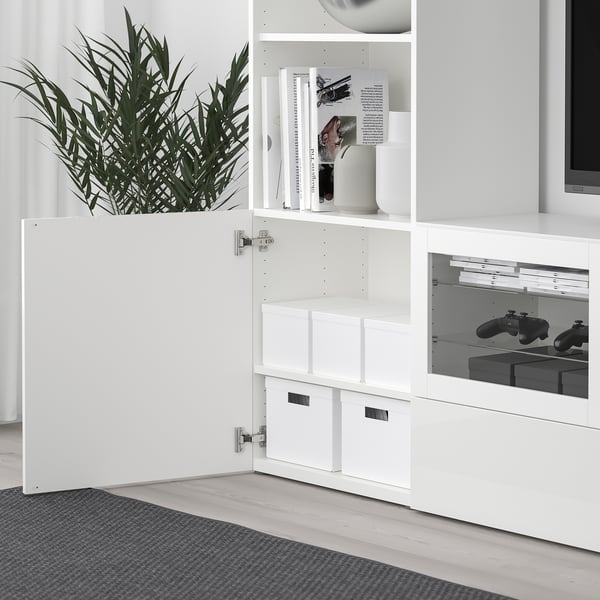 A white TJENA storage unit is shown, with open compartments and drawers, holding gaming controllers.