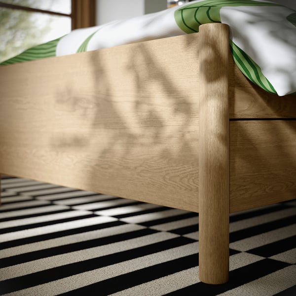 Wooden bed with rounded edges, two drawers, and a striped rug.