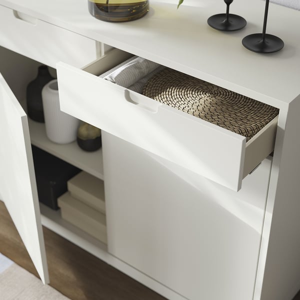 White modern cabinet with open drawer, basket, and decorative items on top.