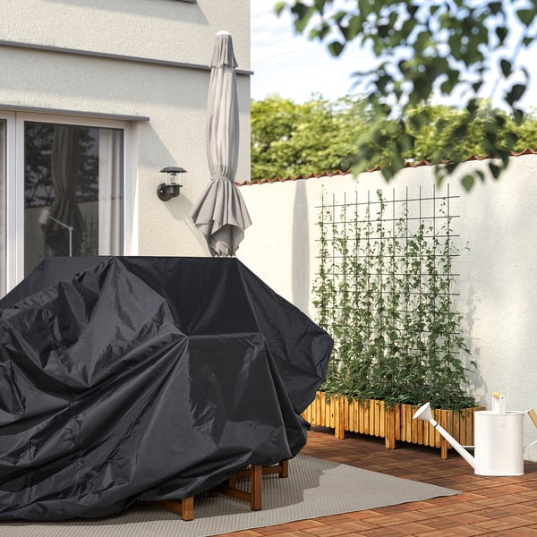Backyard scene: TOSTERÖ cover protects an outdoor table, with a watering can, plants, and glass doors in a serene green setting.