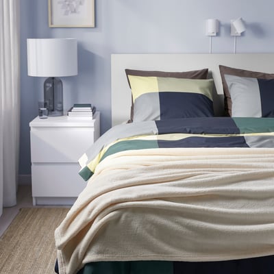 Modern bedroom with striped bedspread on large bed, white headboard, recycled polyester, various cushions.
