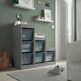 Gray TROFAST storage unit with mesh boxes, holding headphones, bags, and books. It stands tall, reaching the height of the adjacent door.