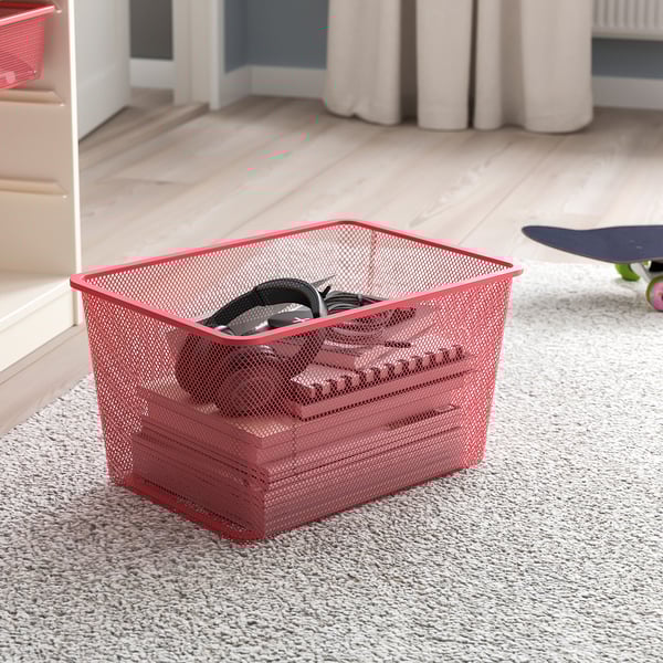 A red mesh basket filled with black headphones rests on a carpeted floor, offering a neat storage solution.