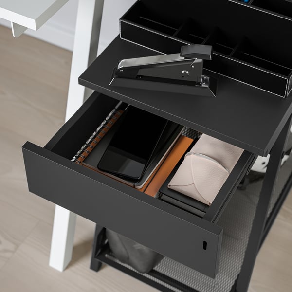 Black TROTTEN storage unit with open drawer revealing wallet, phone, and papers. Lockable, ideal for secure desk or room storage.