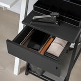 Black TROTTEN storage unit with open drawer revealing wallet, phone, and papers. Lockable, ideal for secure desk or room storage.