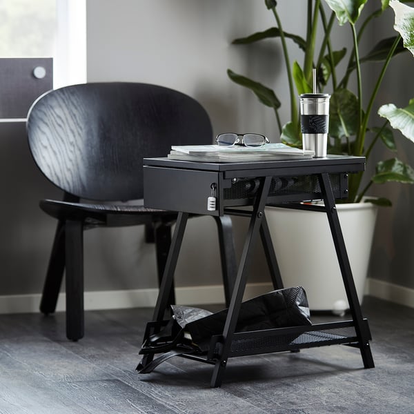 Black TROTTEN storage with drawer, next to plant & chair. Compact, mesh design for desk/sofa. Modern fit.