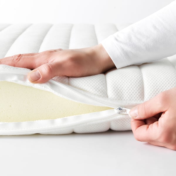 Person zips up white mattress cover, showing easy cleaning feature.