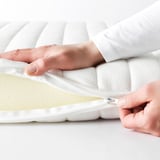Person zips up white mattress cover, showing easy cleaning feature.