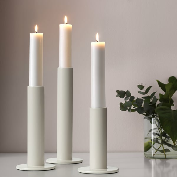 Three lit candles in holders, right vase with greenery.