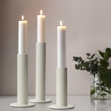 Three lit candles in holders, right vase with greenery.