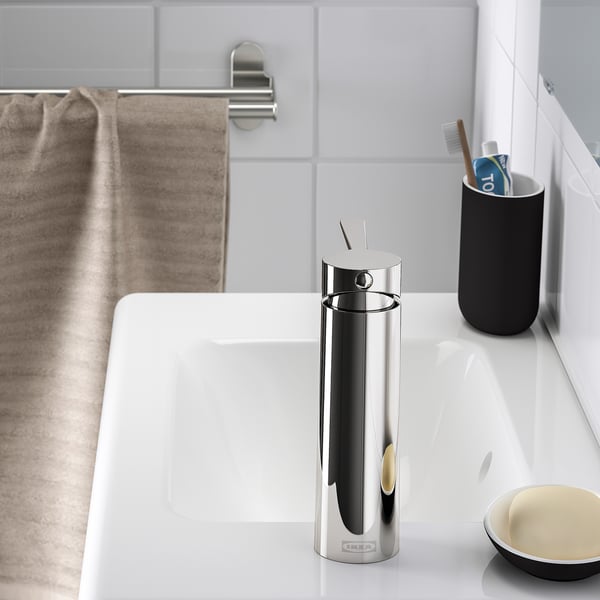 A modern bathroom sink with a sleek tap and black toothbrush holder on a white countertop.
