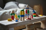 Wooden blocks play area with scattered shapes on bench, bedroom background.