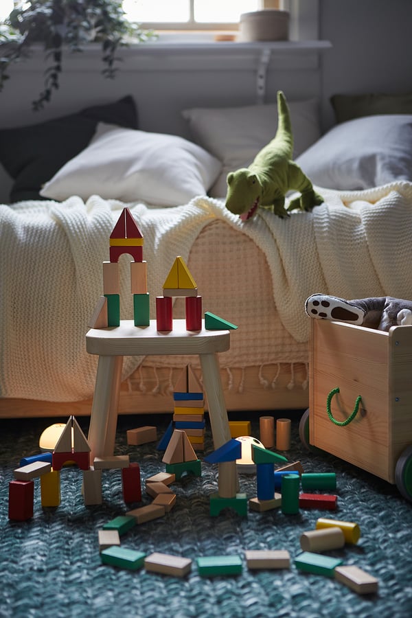 Cozy childs play area, colorful wooden blocks on table, dinosaur toy near bed, blue rug.