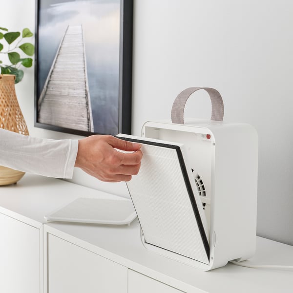 Person handling a white air purifier on a white dresser, showing an easy-to-remove filter.