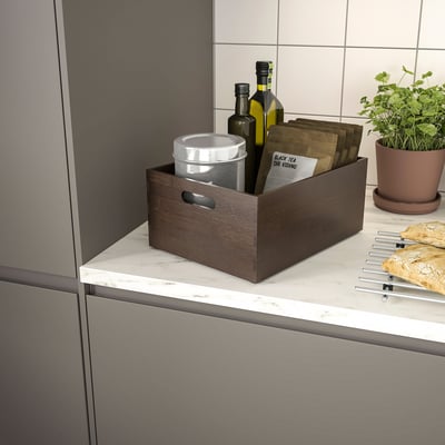 Wooden box on counter holding kitchen items, including bottles and utensils.
