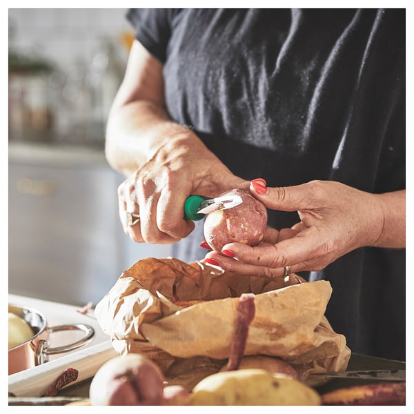 Person peels potato with green UPPFYLLD peeler.