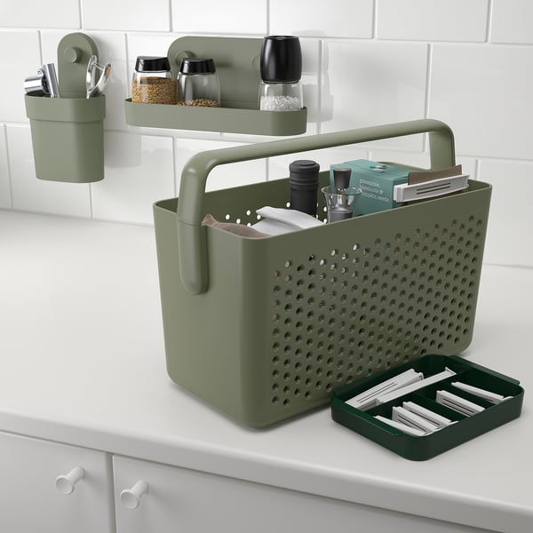 Green storage basket with handle on counter, holding jars, books, and tools. Wall containers store similar items.