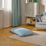 Dog bed on rug, beside grey chair, under window with curtains.
