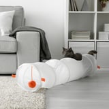 Black cat plays in orange ball cat toy next to sofa with books.