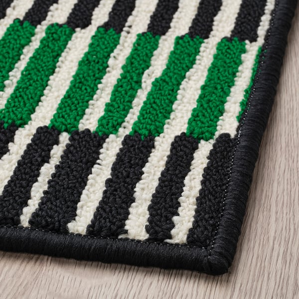 Black, white, and green striped doormat with thick, textured weave lying on a wooden floor.
