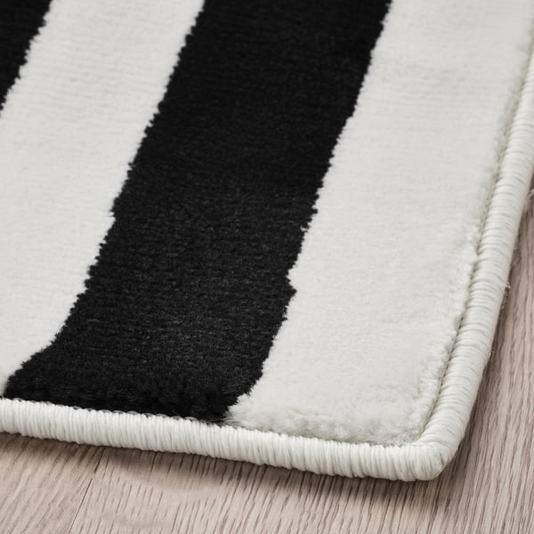 Black and white striped rug on wooden floor. High-quality materials, soft texture, well-crafted edges.