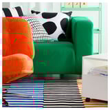 Bright modern room with green sofa, orange chair, and colorful striped rug.