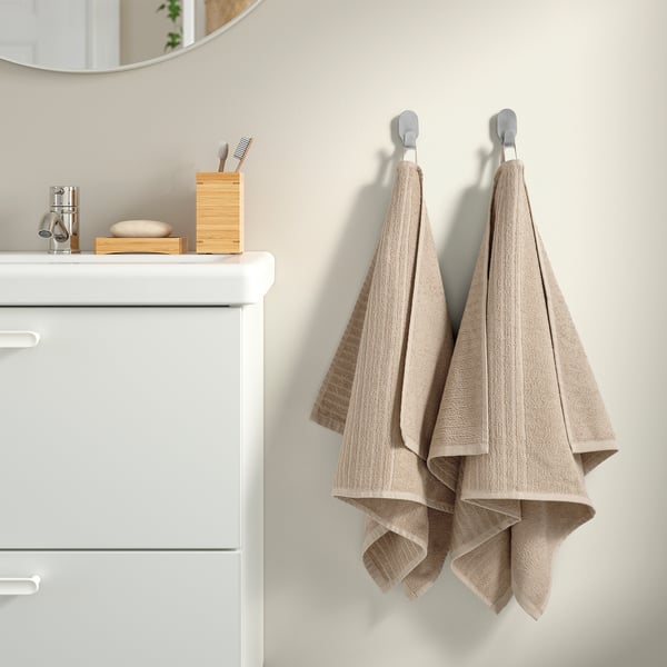 Beige towels on hooks beside sink with toothbrush holder and soap dish.