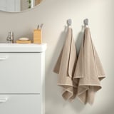 Beige towels on hooks beside sink with toothbrush holder and soap dish.