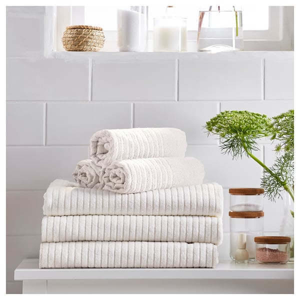 Stacked white VÅGSJÖN towels against gray tiled wall. Topped with woven basket and decorative jars.