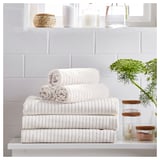Stacked white VÅGSJÖN towels against gray tiled wall. Topped with woven basket and decorative jars.