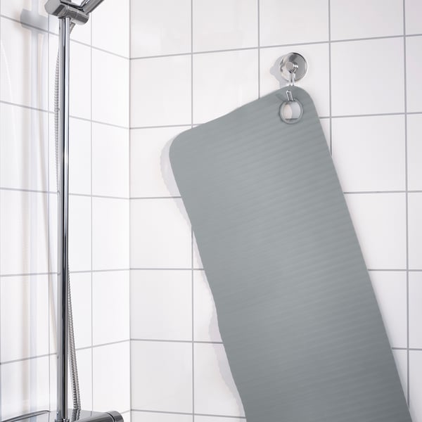 Gray bath mat hangs on wall hook in tiled shower, secured by suction cups.