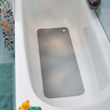 A white bathtub with a blue textured mat, a gray non-slip mat, and floral shower curtain.