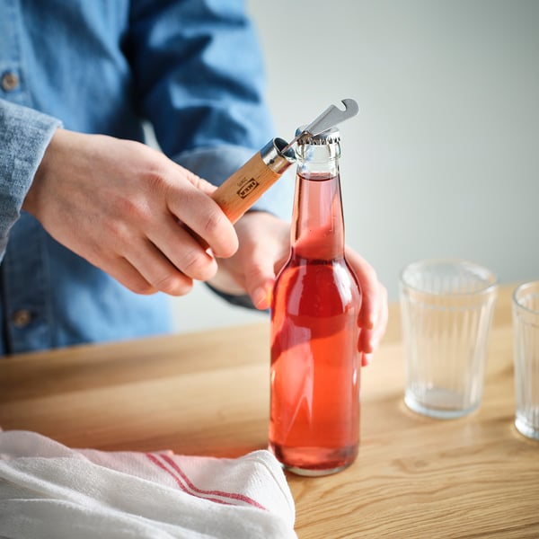 Person opens a bottle with a dual bottle/can opener, its wooden handle providing a firm grip.