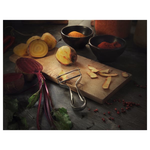 Wooden cutting board with peeler and colorful veggies: red beets, yellow root, green leaves. Spices and peeler.
