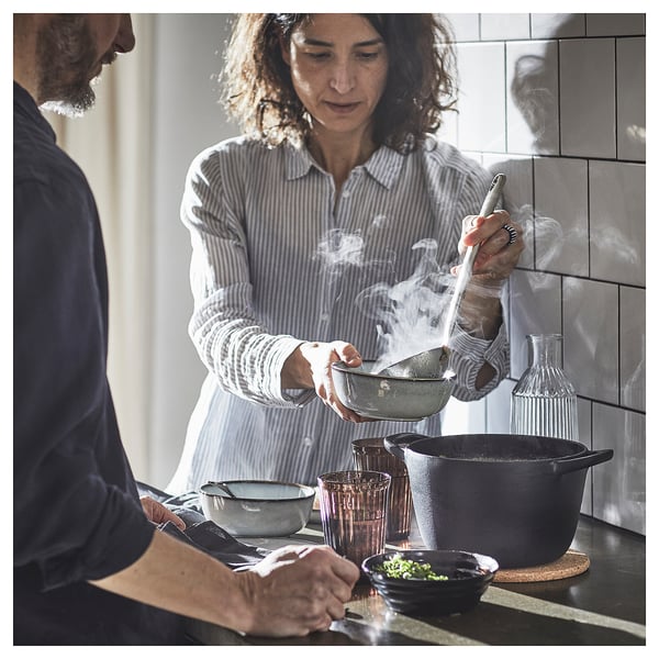 Woman cooks, man observes in modern kitchen.