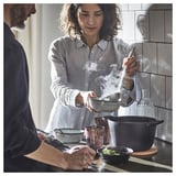 Woman cooks, man observes in modern kitchen.
