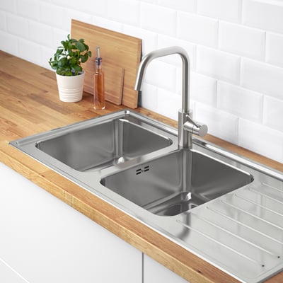 Stainless steel kitchen sink with faucet and drainboard. A reversible drainboard and built-in sound reduction material.