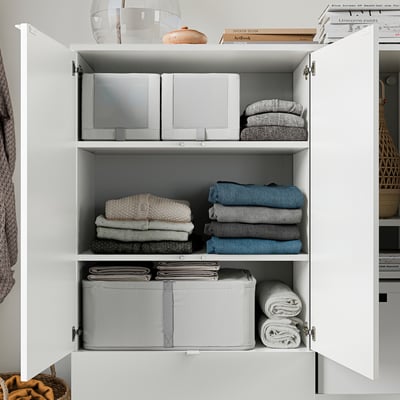 Organized closet with white shelves, neatly folded clothes, and decorative items.