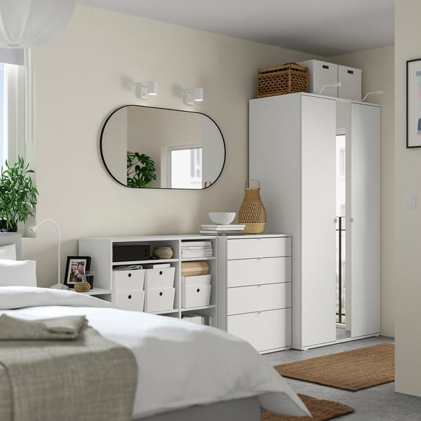 Modern white bedroom with a wardrobe, chest, mirror, and natural decor. Clean and minimalist design.