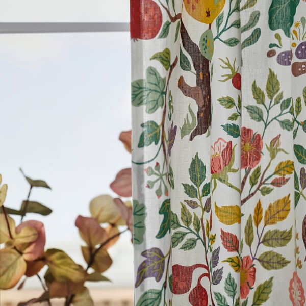Bright floral curtains hang by a window, filtering light with vibrant designs. A plant sits in the foreground, enhancing the rooms decor.