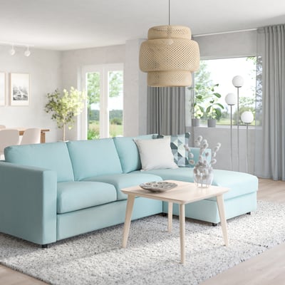 Modern living room: l-shaped sofa, coffee table, large window, plants, rug, hanging light.