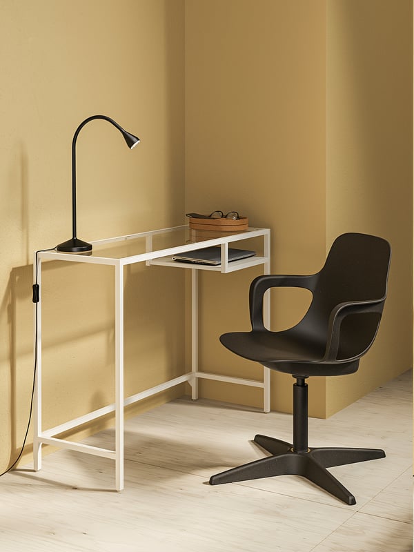 Modern home office setup with white VITTSJÖ laptop table, black desk lamp, and black swivel chair against mustard walls.