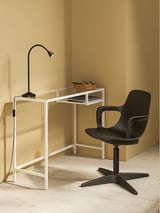 Modern home office setup with white VITTSJÖ laptop table, black desk lamp, and black swivel chair against mustard walls.