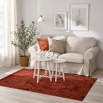 Cozy living room with beige VONSBÄK sofa, orange/white cushions, red rug, table, plant, warm decor.