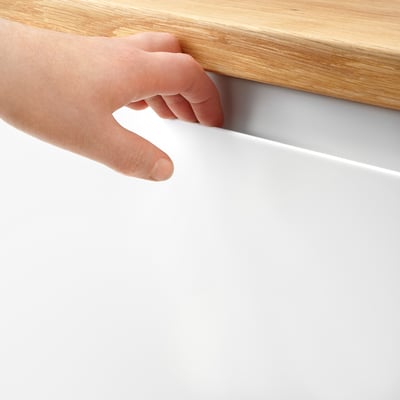 A hand opening a white cabinet door, showcasing VOXTORPs integrated handle and smooth surface.